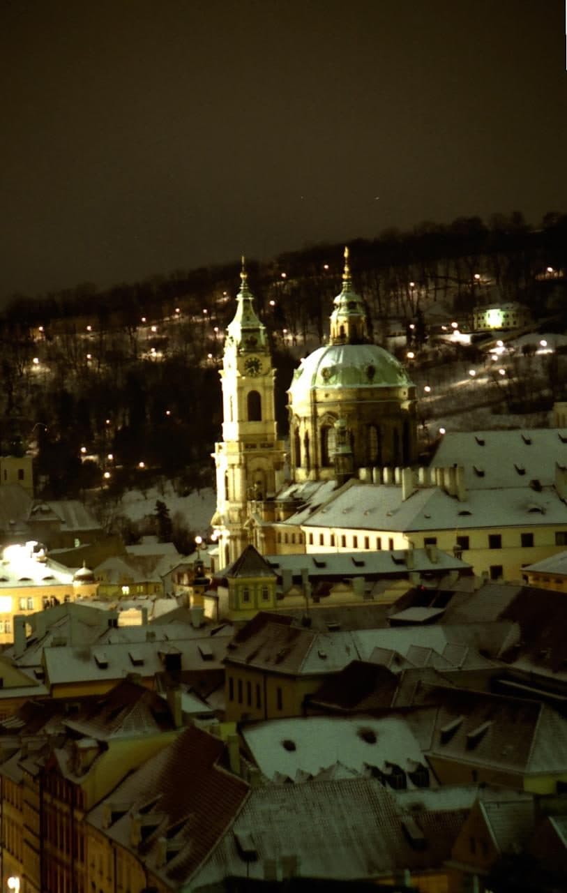 Prag bei Nacht, ein Kirchturm über verschneiten Dächern
