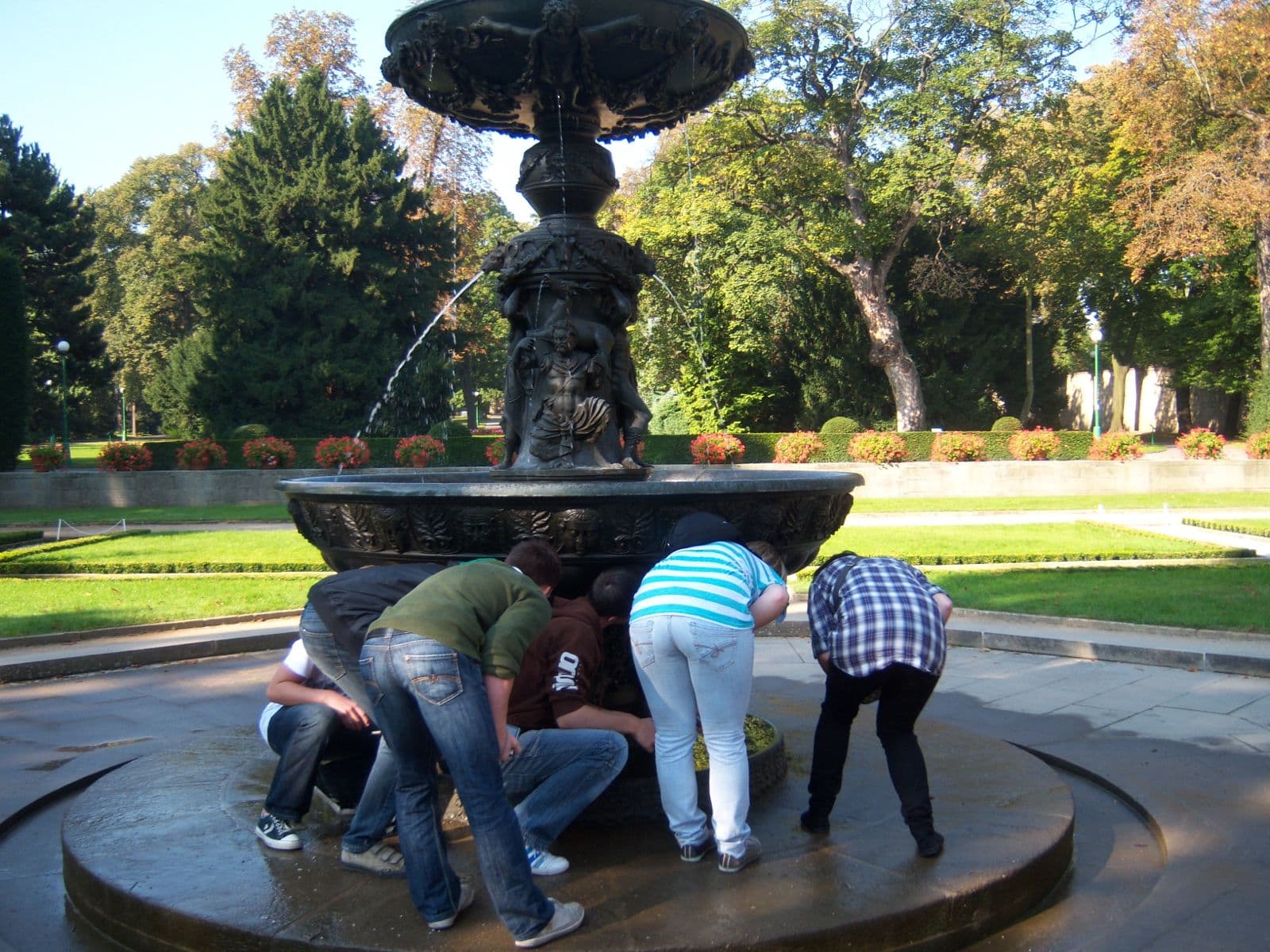Schüler beugen sich über den Rand eines Brunnens in einem Prager Park