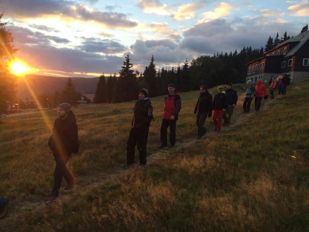 Konferenzteilnehmer gehen bei Sonnenuntergang einen grasbewachsenen Hang zum Berghotel hinunter